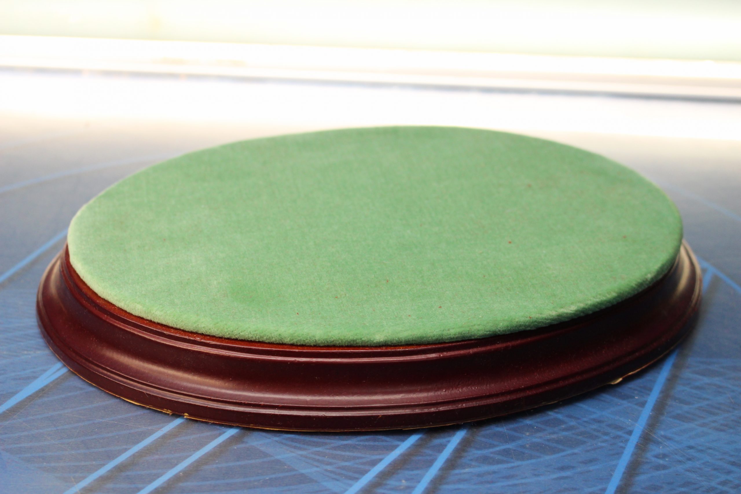 Peana ovalada de madera chocolate y terciopelo verde.